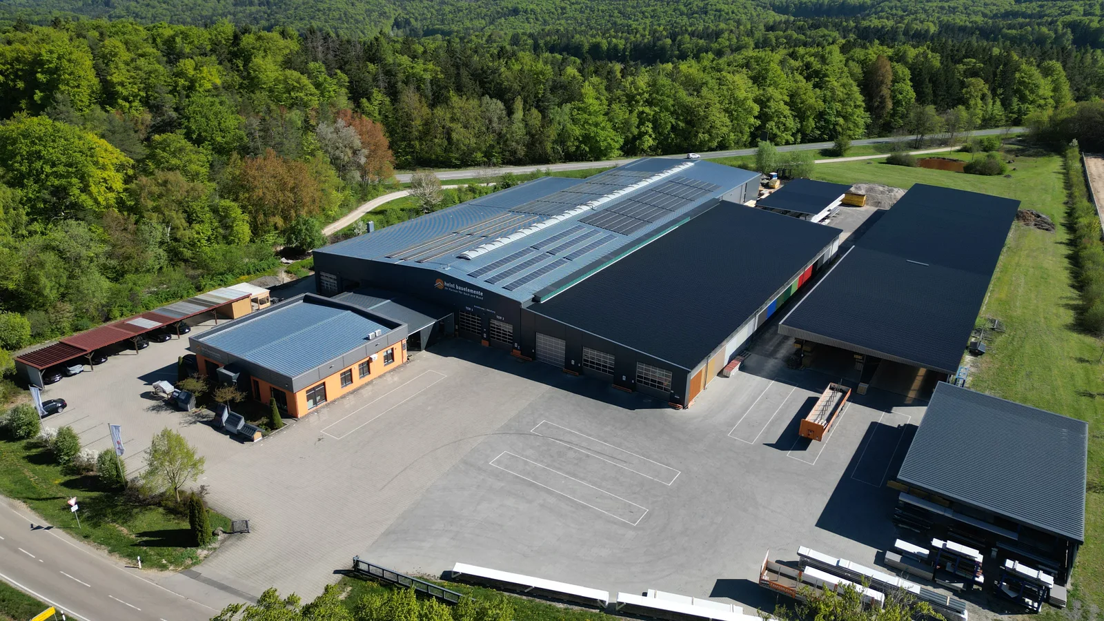 Luftbild des Firmensitzes von heinl stahlkonstruktionen und heinl bauelemente in Illschwang-Neuöd, Oberpfalz: Stahlhallen mit Photovoltaik am Waldrand